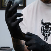 Tattoo artist in a white Demons t-shirt pulling on black nitrile gloves