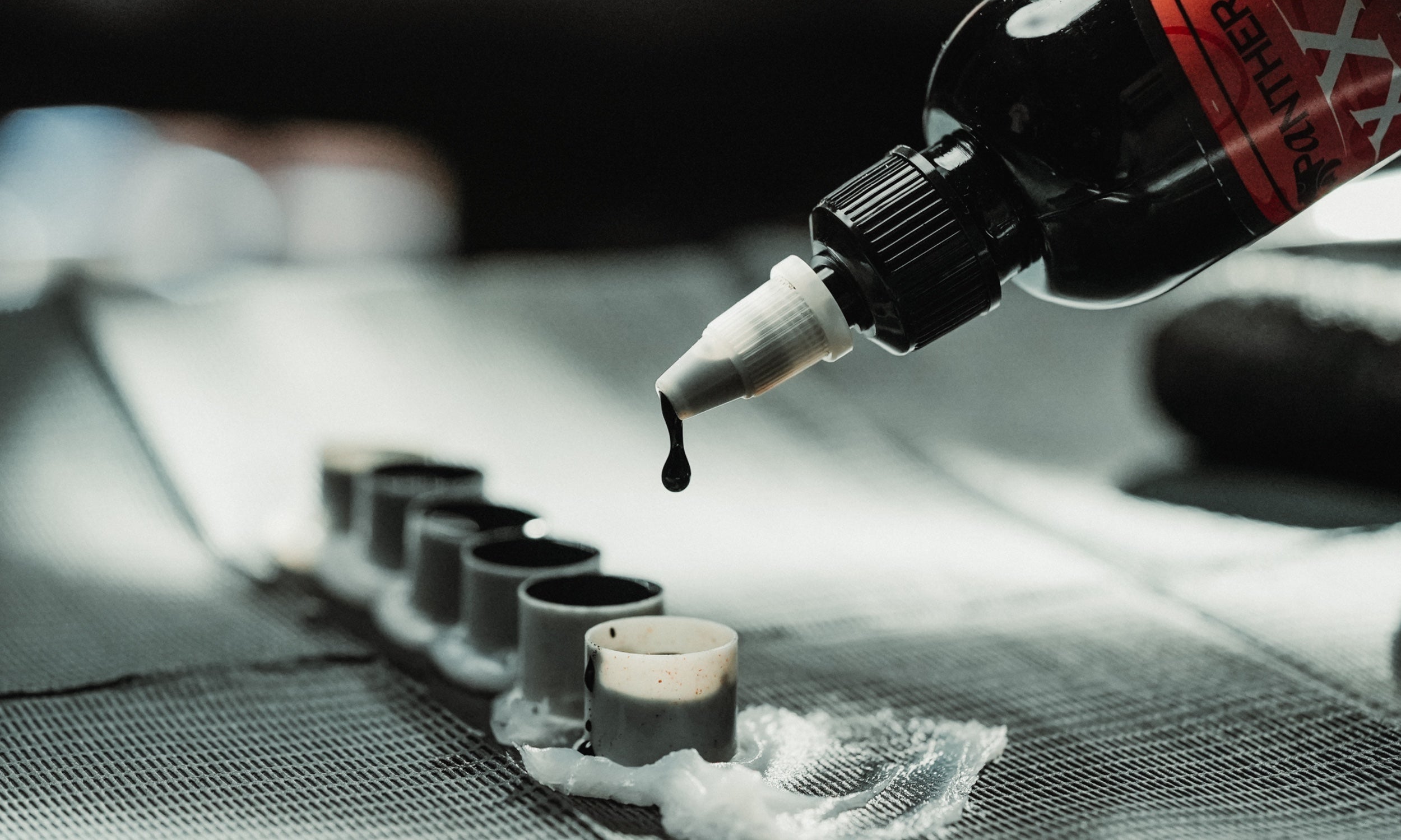 Black Panthera ink poured from the XXX bottle into ink caps at a tattoo station