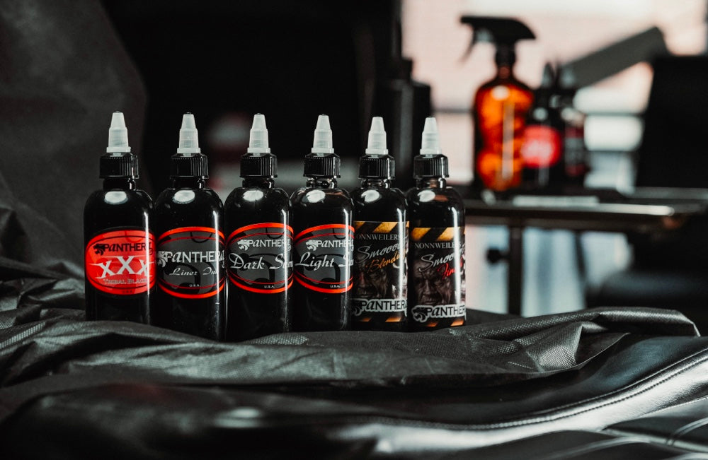 Six Panthera ink bottles set out on a black studio workstation next to a tattoo machine