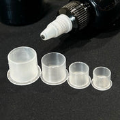 Four sizes of clear Demons ink caps on a dark bench under a tattoo machine tip